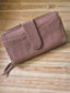 A dusty rose pink zip-around wallet with a textured, vertically ribbed fabric and a matching tassel zipper pull, displayed diagonally on a light-colored wooden plank surface.