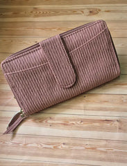 A dusty rose pink zip-around wallet with a textured, vertically ribbed fabric and a matching tassel zipper pull, displayed diagonally on a light-colored wooden plank surface.