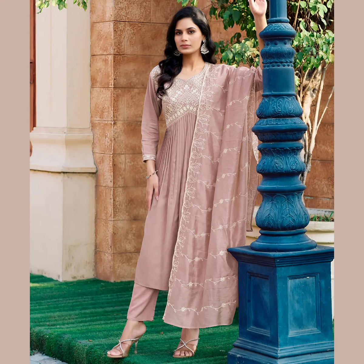 Woman in a pink traditional outfit standing next to a blue decorative post outdoors. Main image
